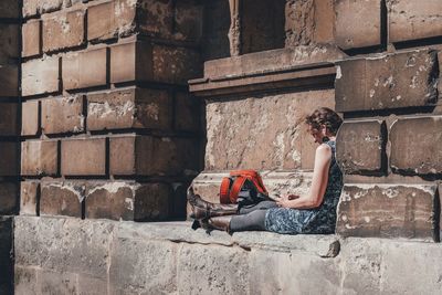 Woman sitting on steps against brick wall