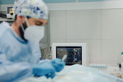 Focused male veterinarian in uniform and respiratory mask using medical instruments during surgery in hospital