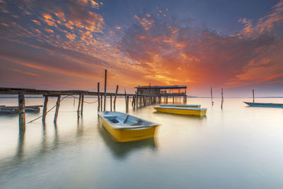 Boats moored on sea against sky during sunrise