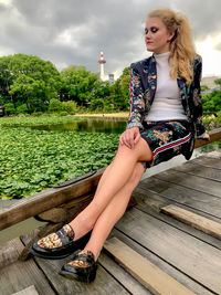 Young woman looking away while sitting on plant against sky