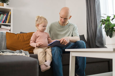 Side view of mother and daughter sitting on sofa at home