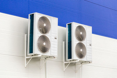 Two double condensing units of air conditioner on blue and white metal industrial wall.