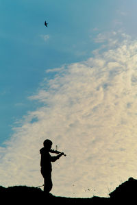 Low angle view of silhouette woman playing violin on mountain against sky