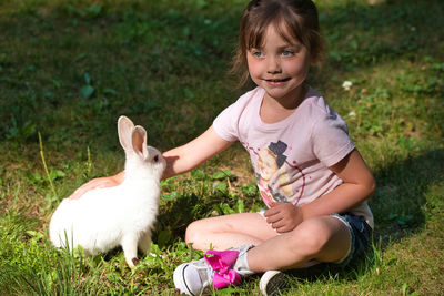 Cute girl playing with rabbit while sitting on field