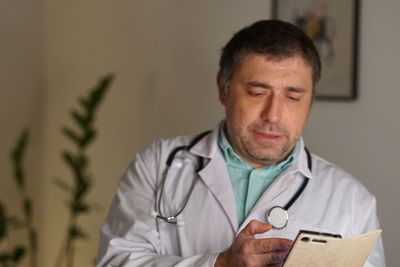 Close-up of mature doctor using phone against wall