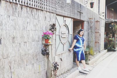 Full length of woman standing by wall of building