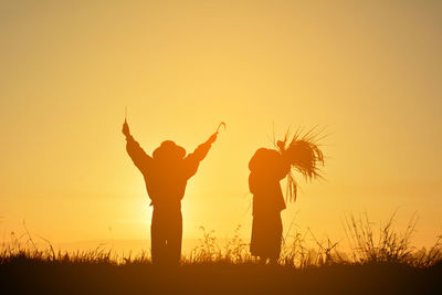 Silhouette friends standing on field against clear sky during sunset