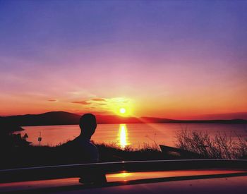 Silhouette woman by lake against sky during sunset