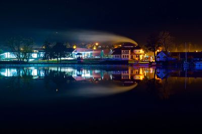 Illuminated buildings by river against sky at night