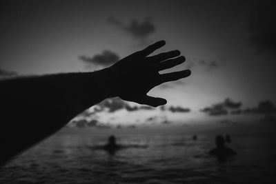 Silhouette person hand by sea against sky during sunset