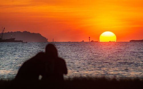 Silhouette man standing by sea against orange sky