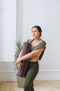 Portrait of young woman standing against wall at home