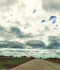 Vehicles on road against cloudy sky