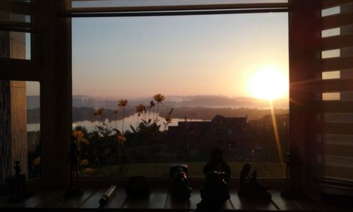 Silhouette people photographing sunset seen through window