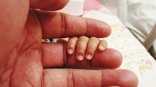 Cropped hand of woman with baby on bed