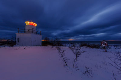 Lighthouse on snow covered landscape against sky at sunset