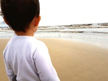 Rear view of boy standing on beach against clear sky