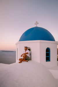 Man sitting by church against sky