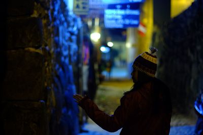 Rear view of woman standing in illuminated alley at night