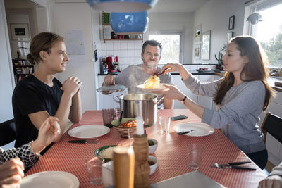 Woman serving food in plate while sitting with family at dining table