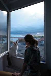 Rear view of young woman looking through window