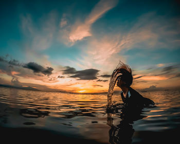 Woman tossing hair in sea against sky during sunset