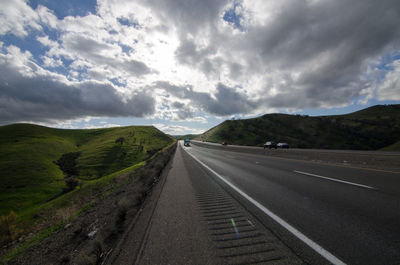 Road passing through landscape against cloudy sky