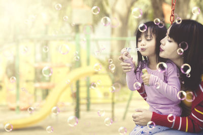 Mother and girl blowing bubbles at park