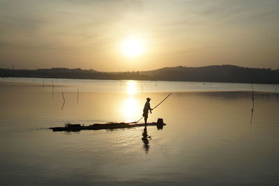 Silhouette man in lake against sky during sunset