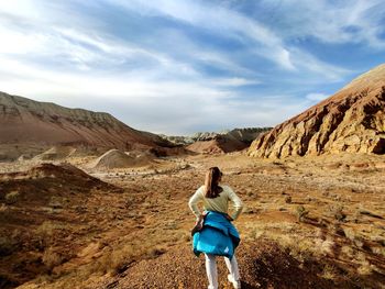 Rear view of woman standing on rock against mountains and sky