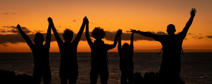 Silhouette people with arms raised at beach during sunset