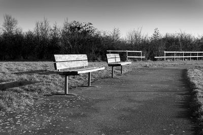 Empty benches against trees on landscape against sky