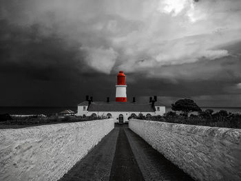 Lighthouse on beach against cloudy sky
