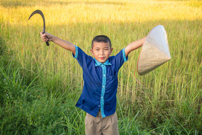 Portrait of boy holding hat and sickle on field