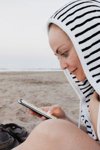 Side view of woman using smart phone sitting at beach