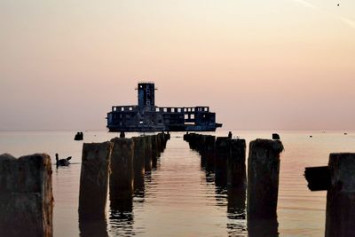 Wooden posts in sea against sky during sunset