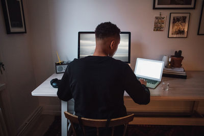 Rear view of young freelance worker using laptop and computer at desk