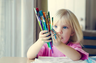 Close-up portrait of girl with paintbrushes at home