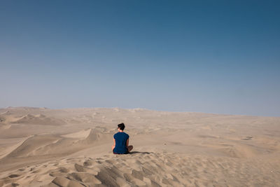 Rear view of man on sand dune in desert against clear sky