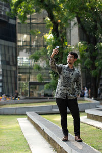 Young man with batik shirt takes a selfie at a park