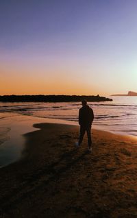 Rear view of silhouette man standing on beach during sunset