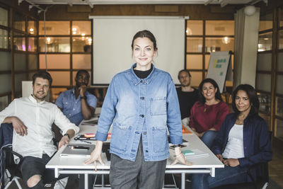 Portrait of confident businesswoman standing by coworkers sitting in board room at office