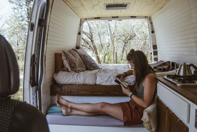 Side view of woman reading book while sitting on seat in motor home