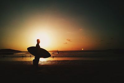 Silhouette man with surfboard on beach at sunset