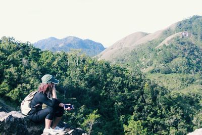 Side view of woman holding smart phone while sitting on mountain