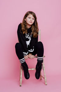 Portrait of young woman sitting against pink background