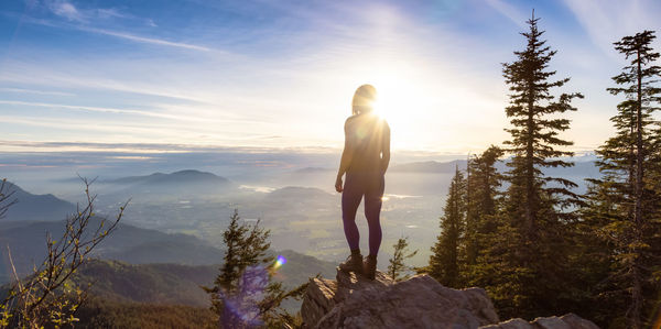 Rear view of woman standing on rock against sky