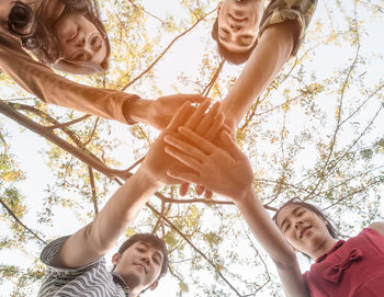 Low angle view of friends stacking hands against trees