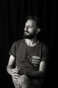 Mid adult man looking away while sitting against black background