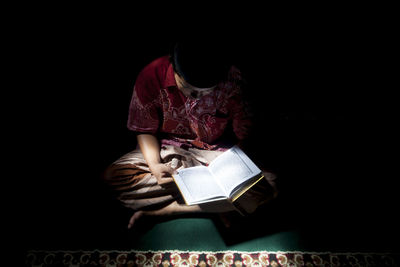 Midsection of woman reading book against black background